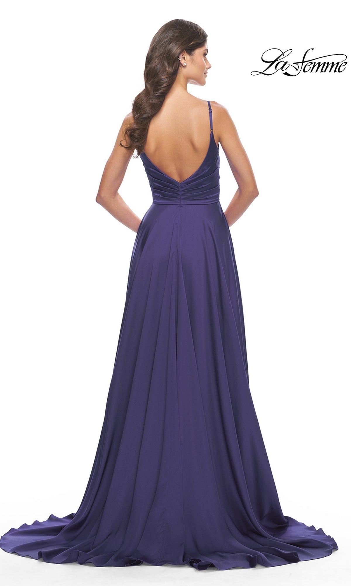A woman with long wavy hair models the La Femme Open-Back A-Line Designer Prom Dress 31233 in deep purple, featuring thin straps and a low V-back, against a white background.